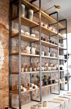 a brick wall with shelves filled with pots and vases next to a table topped with dishes