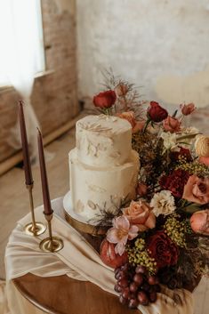 a white wedding cake sitting on top of a table next to a candle and flowers