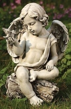 an angel statue sitting on top of a tree stump holding a bird in its hand