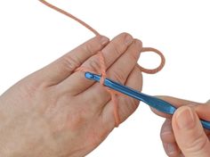 someone crocheting an orange string with a blue handled knitting needle, while another person holds the yarn in their hand