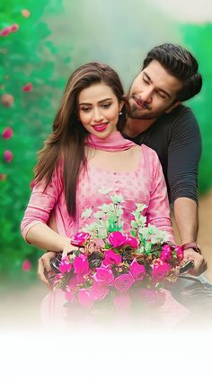 a man and woman embracing each other in front of pink flowers with green foliage behind them