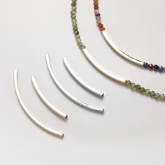 four necklaces with different colored beads and metal bar ends on a white table top