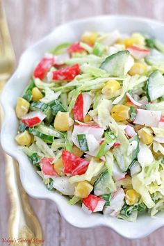 a salad in a white bowl on top of a wooden table next to a fork