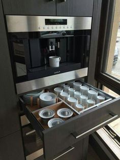 an open drawer in a kitchen with plates and cups on the bottom shelf, next to a coffee maker