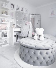 a white bedroom with a round ottoman and teddy bear