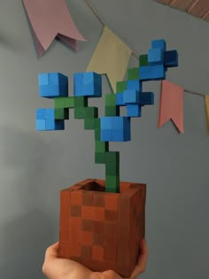 a hand holding a small plant made out of lego blocks and colored paper streamers