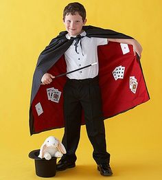 a young boy in a tuxedo and magician outfit holding up a red cape with playing cards on it