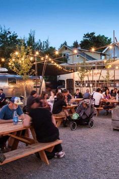 many people are sitting at picnic tables in front of food trucks and camper trailers