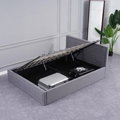 an open gray box with silver items inside on the floor next to a plant and mirror