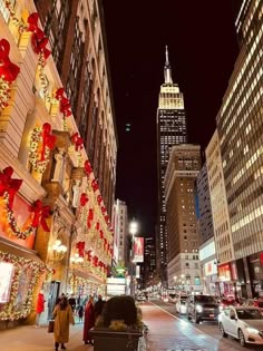 people are walking down the street with christmas decorations on buildings in the city at night