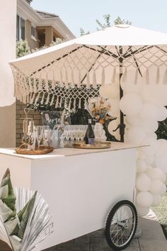 an outdoor bar set up with balloons and wine glasses on the table, next to a white umbrella