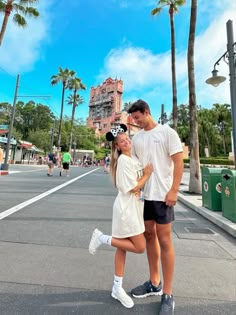 a man and woman are standing in the middle of an empty street with palm trees