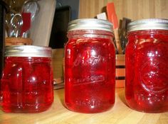 three jars filled with red liquid sitting on top of a wooden table