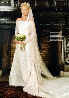 a woman in a white wedding dress and veil standing next to a fire place with flowers