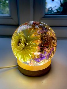 a glass ball with flowers in it sitting on a table next to a window sill