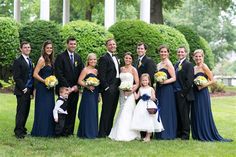 a group of people standing next to each other in front of trees and bushes at a wedding