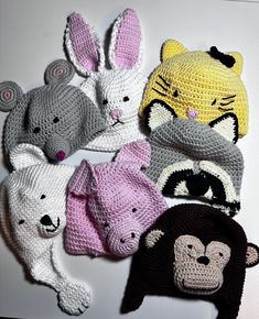 several crocheted animal hats are arranged on a white surface, with one wearing a hat and the other holding a stuffed animal