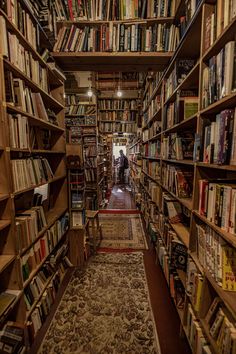 a narrow bookshelf filled with lots of books and people in the distance walking through it