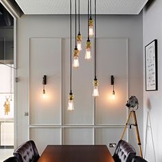 a table with chairs and lights hanging from the ceiling in an office space that has white walls