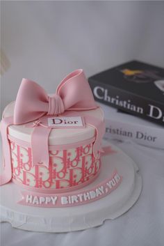 a birthday cake with a pink bow on top and a christian dior book in the background