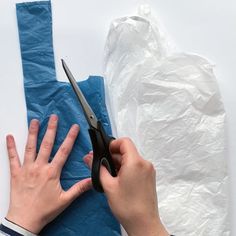 someone using scissors to cut paper on a piece of blue cloth with white background and plastic bag