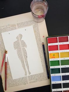 the paper is cut out to look like a man's body, with paint and pencils next to it