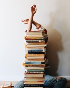 a person sitting on the floor with a stack of books in front of their head