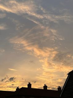 an airplane flying in the sky at sunset with clouds above it and some buildings below