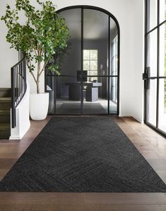 a large black rug in the middle of a room next to a stair case and potted plant