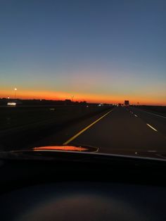 the sun is setting on an empty highway as seen from inside a vehicle's dashboard