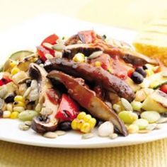 a white plate topped with meat and veggies next to corn on the cob