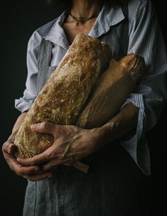 a woman holding two large loafs of bread in her hands on a black background