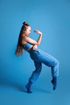 a woman in blue jumpsuits is doing a kick - up on a blue background