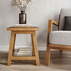 a small wooden table with books on it next to a chair and flower arrangement in a vase