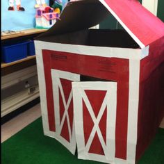 a red and white barn made out of paper on green carpeted area with toys in background