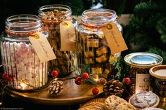 several jars filled with candy and cookies next to christmas decorations on a wooden platter