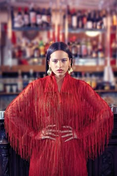 a woman in a red dress with fringes on her shoulders, standing at a bar