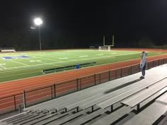 a person standing on the bleachers at night in front of an empty football field