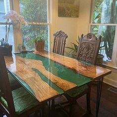 a wooden table with green glass top in front of a window and potted plants