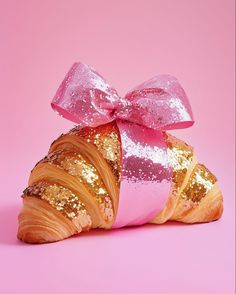 a croissant wrapped in pink and gold sequins with a bow on top