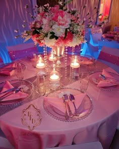 the table is set with silverware and pink napkins, candles and flowers in vases