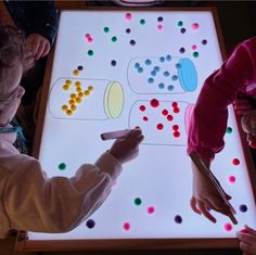 two children are playing with colored dots on a projected surface while another child looks at them