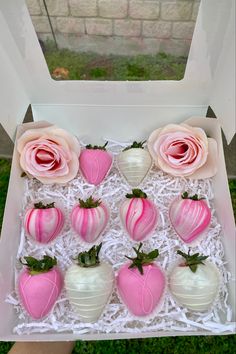 a box filled with pink and white chocolate covered strawberries sitting on top of green grass