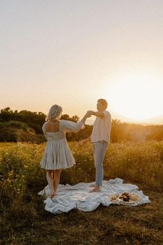 a man and woman standing on top of a blanket in the middle of a field