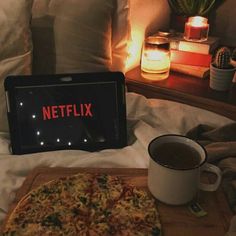 a laptop computer sitting on top of a bed next to a cup of coffee and a pizza