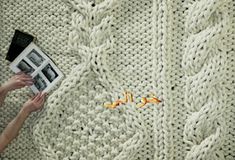 a woman is knitting a sweater on the floor with her feet propped up and holding an open magazine