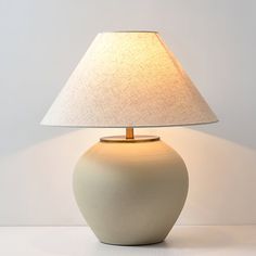 a white table lamp with a beige shade on it's base and a light bulb in the middle