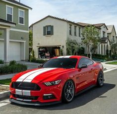 a red and white mustang parked in front of some houses