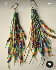 two pairs of multicolored beaded earrings hanging from hooks on a white surface