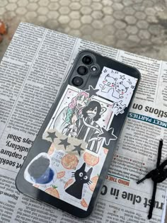 an iphone case with stickers on it sitting on top of a newspaper next to scissors